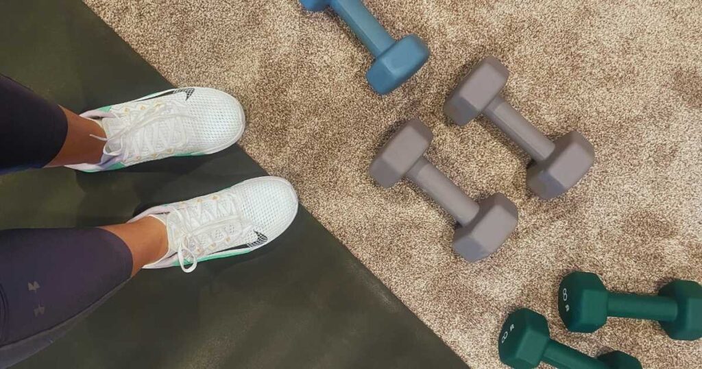 nike metcon athletic shoes on workout mat near dumbbells