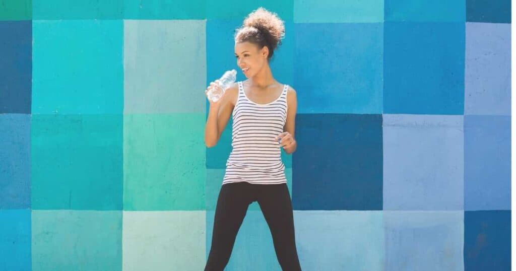 woman against colorful blue wall drinking water