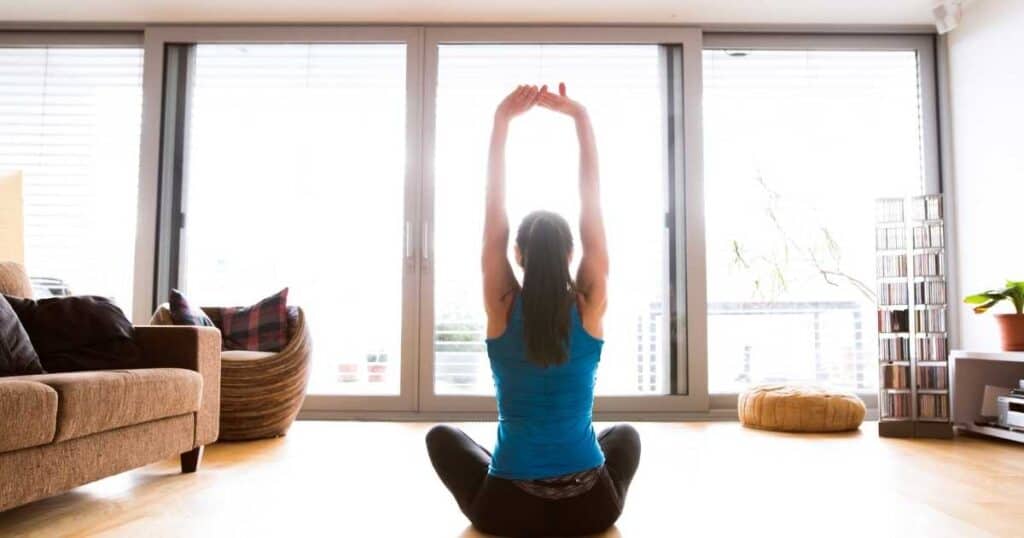 woman stretching in sunlit room in front of windows