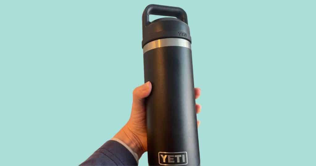 hand holding yeti water bottle blue background