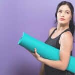 purple background woman holding blue yoga mat