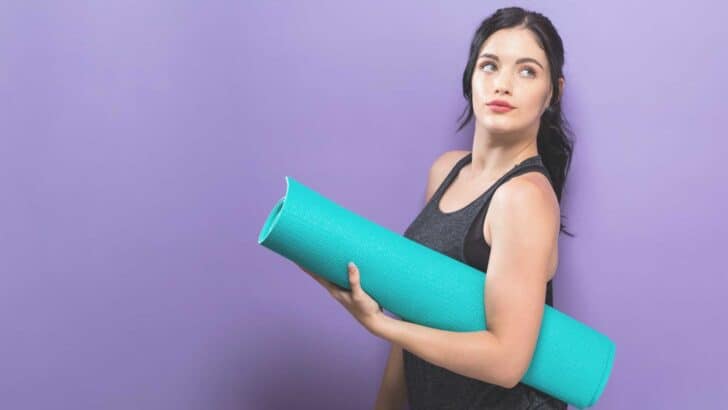 purple background woman holding blue yoga mat