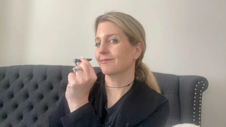 woman smiling at camera holding Komuso Shift necklace sitting on gray couch