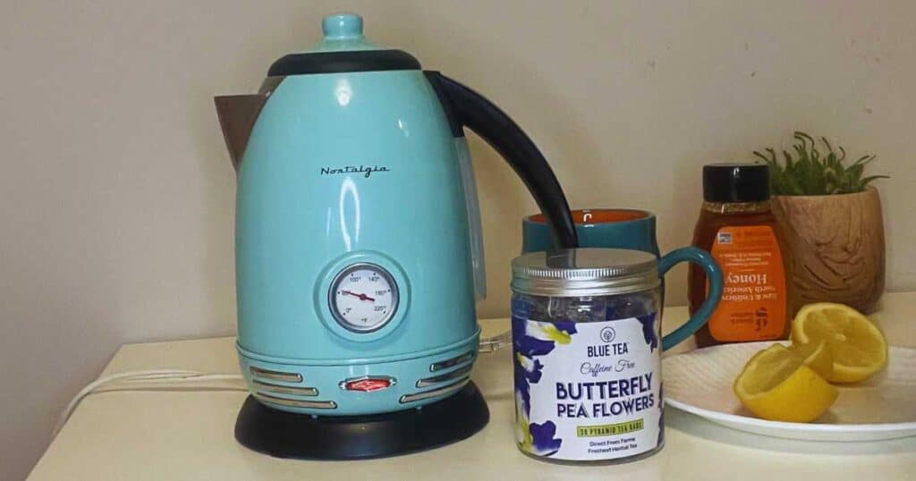butterfly pea flowers tea next to honey, lemon, and an electric tea kettle