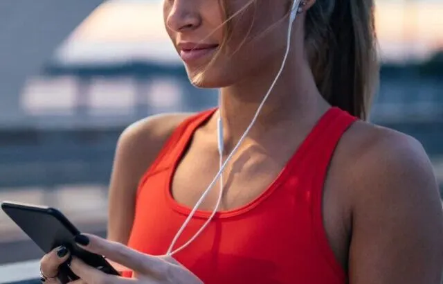 fit woman in red sports bra with headphones and smartphone