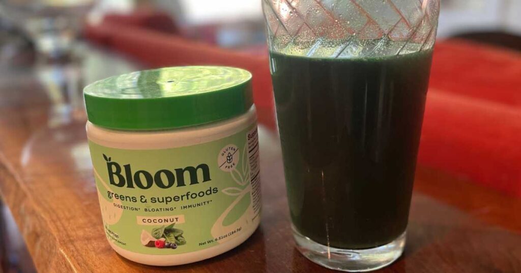 Container of Bloom Supergreens next to glass on wood table