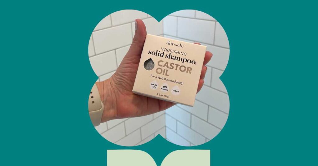 teal background clover shaped frame hand holding kitsch shampoo bar in a box against white tiles