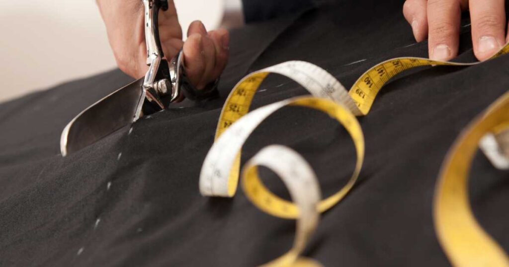 tailor cutting black fabric next to measuring tape