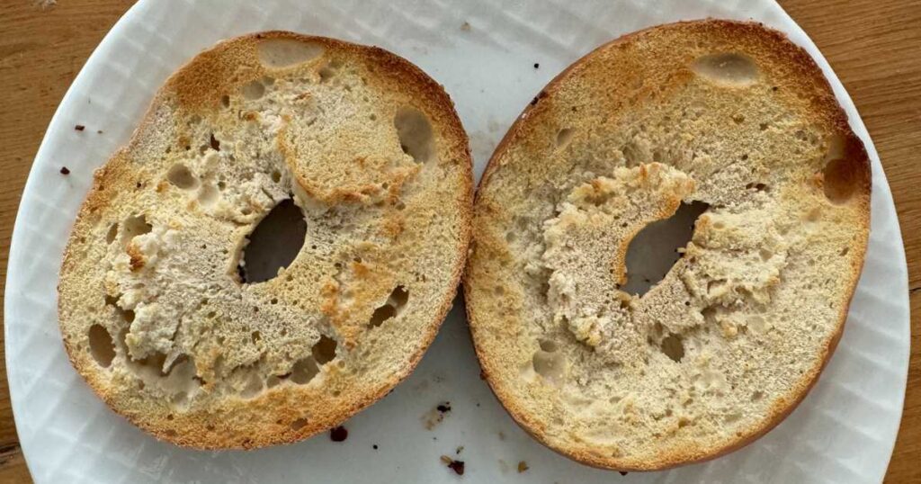 better bagel split in half toasted sitting on a white plate on a wooden table.