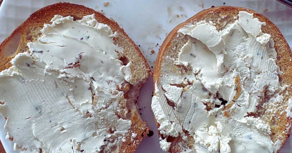 cream cheese spread on the better bagel on a white plate.