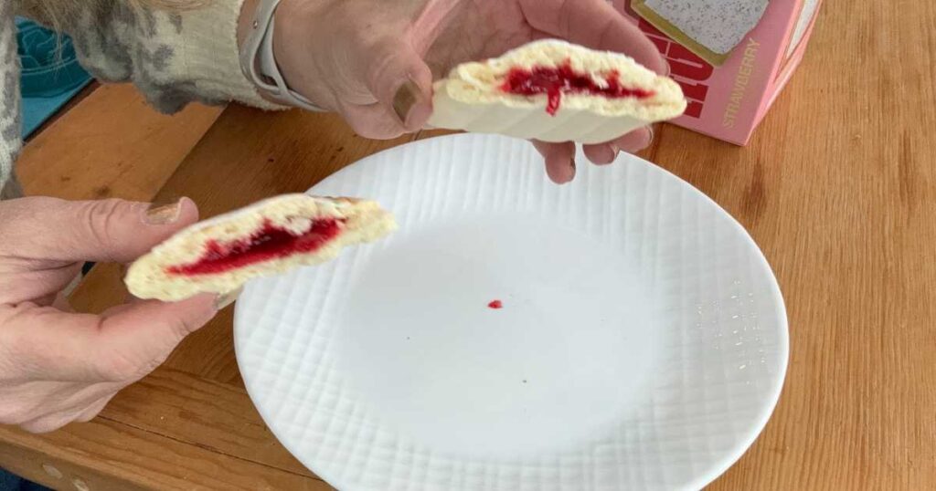 Hands holding strawberry Legendary Protein Pastry broken in half over white plate.