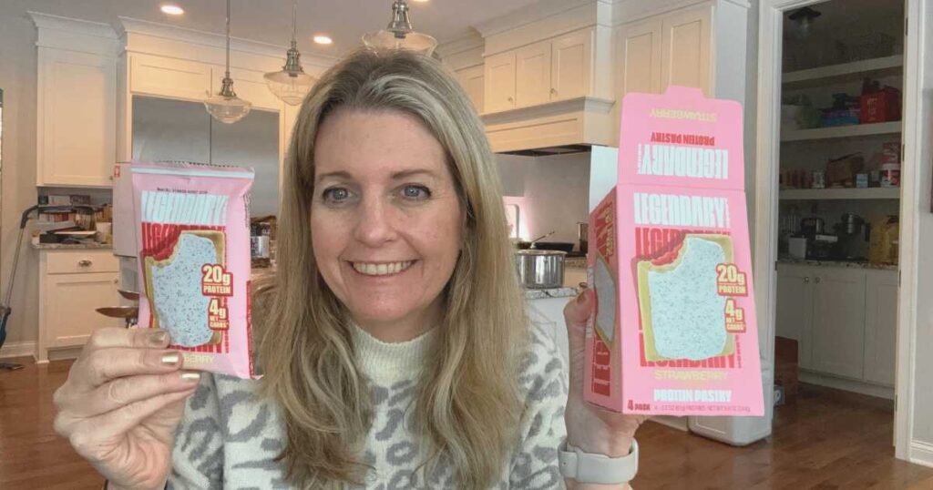 Michelle Platt holding a box of Legendary Protein Pastry and package smiling in front of white kitchen.