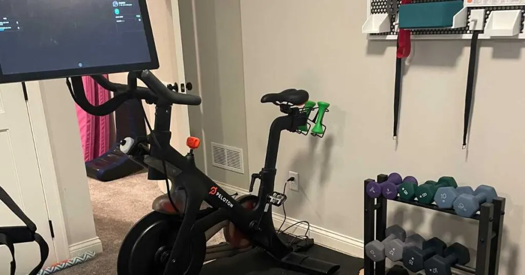 peloton bike with screen tilted next to rack of dumbbells. 