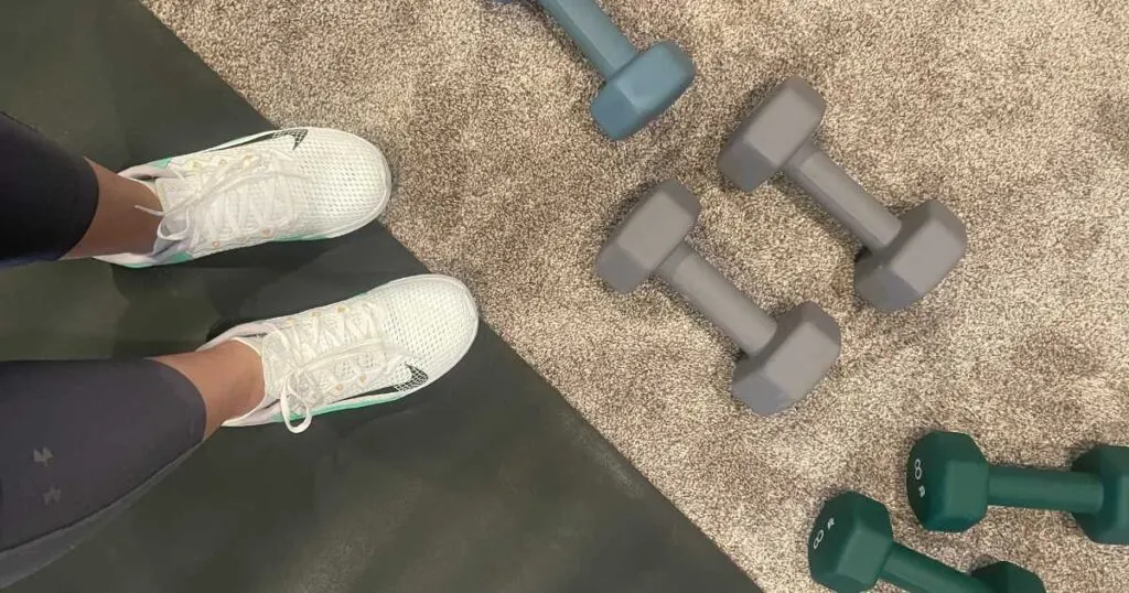 dumbbells on a carpet next to an exercise mat and shoes