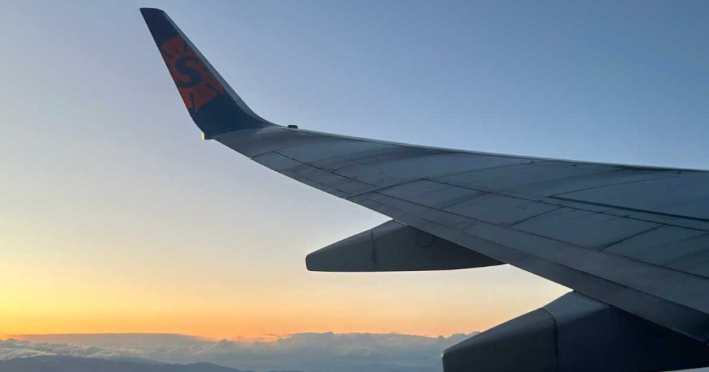 suncountry airplane wing with sunset sky and clouds underneath.