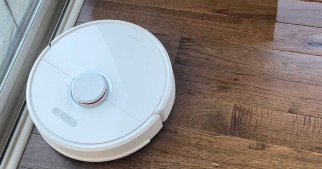 white roborock robot vacuum mopping and vacuuming dark hardwood floors.