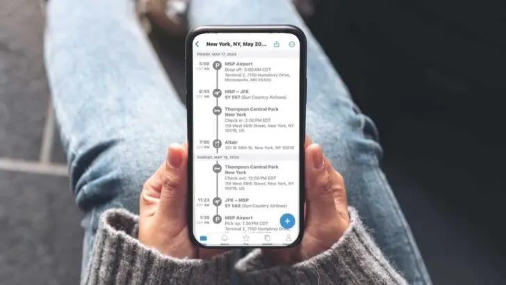 woman holding an iphone on her lap wearing jeans displaying a tripit app itinerary.