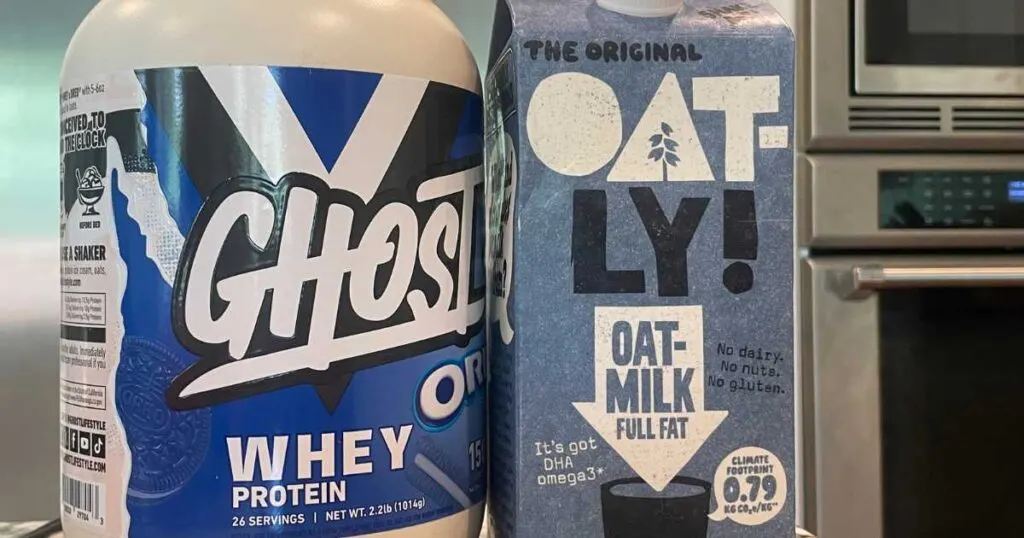 Large container of Ghost oreo whey protein next to a container of Oatly oat milk microwave in background