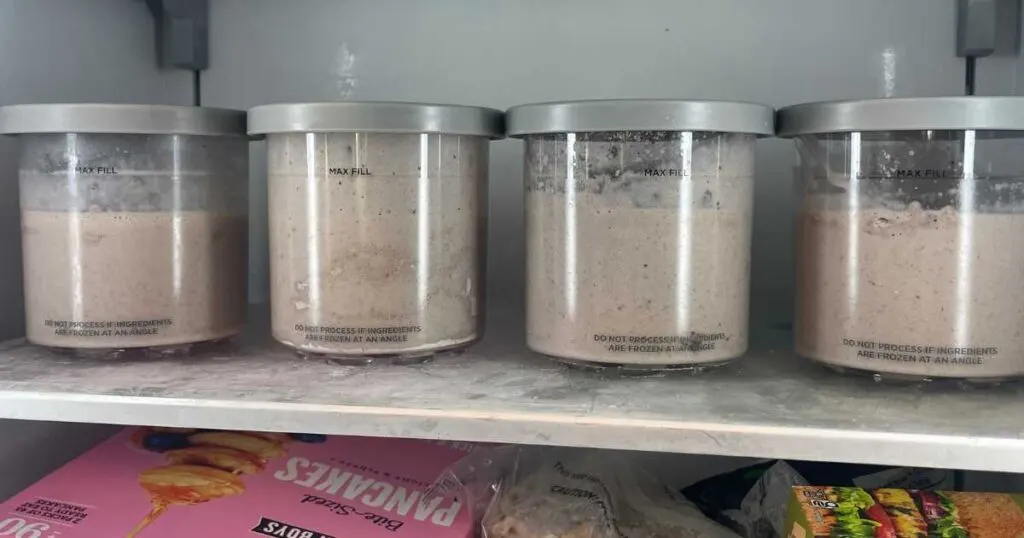 Four Ninja Creami containers in a line on freezer shelf.