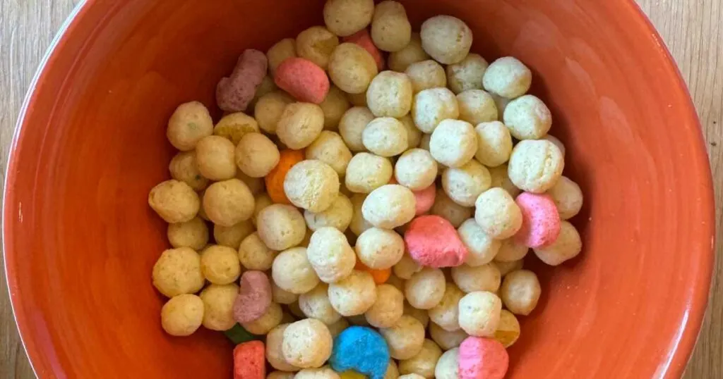 Orange bowl on wooden table with round Ghost protein cereal and colorful marshmallow pieces in it.